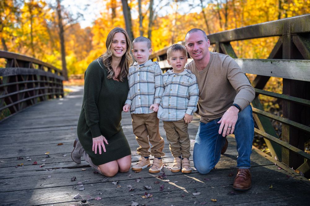 A casual family portrait taken on a rustic wooden bridge during golden hour.