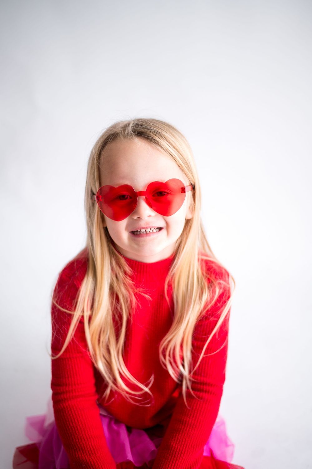 Four sequential photos showing someone wearing a red turtleneck sweater and heart-shaped sunglasses against a white background.