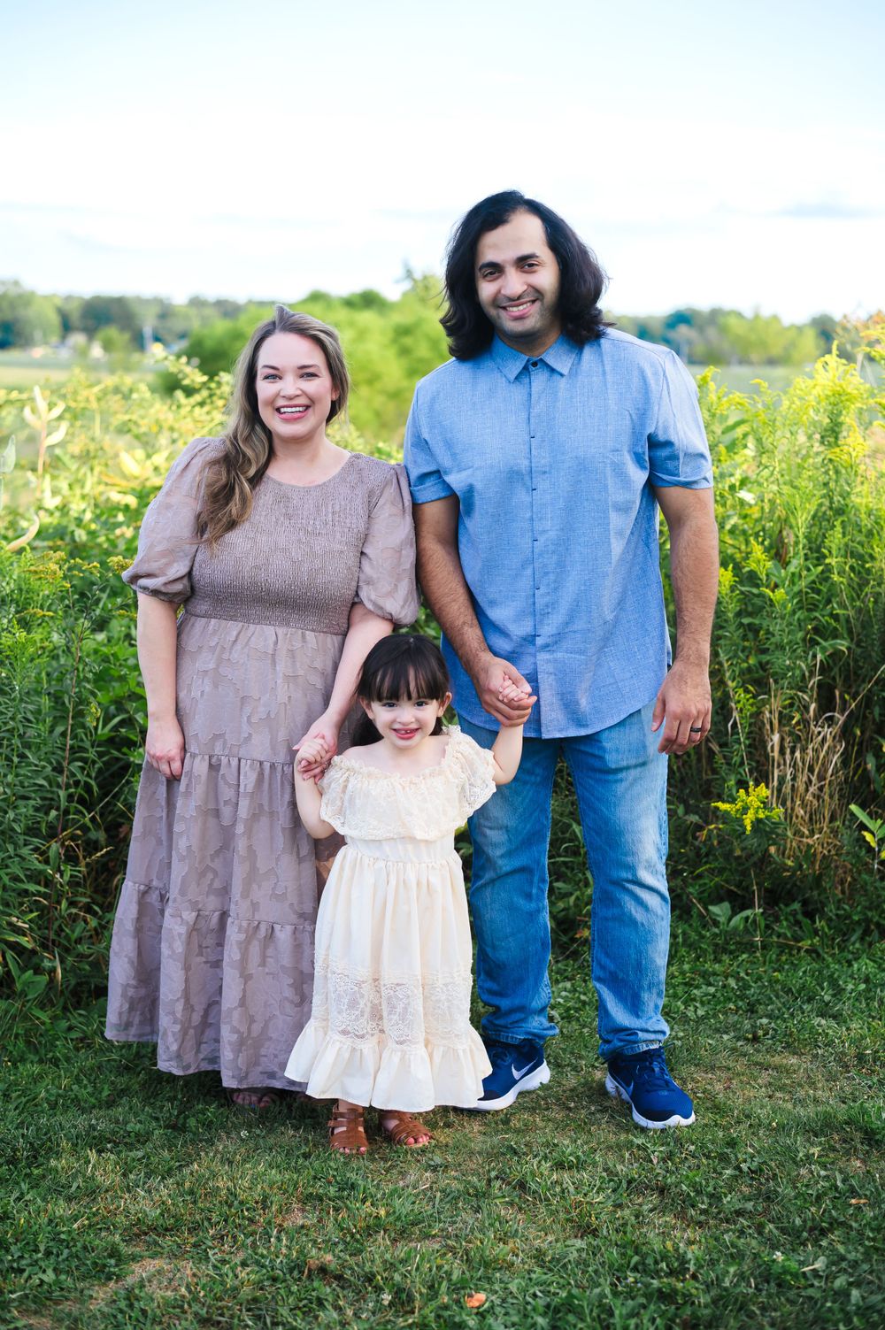 A family of three poses together in a wildflower field during golden hour.