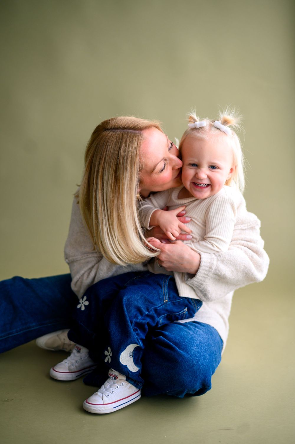 A heartwarming moment of affection and laughter between parent and child wearing matching light sweaters and jeans.