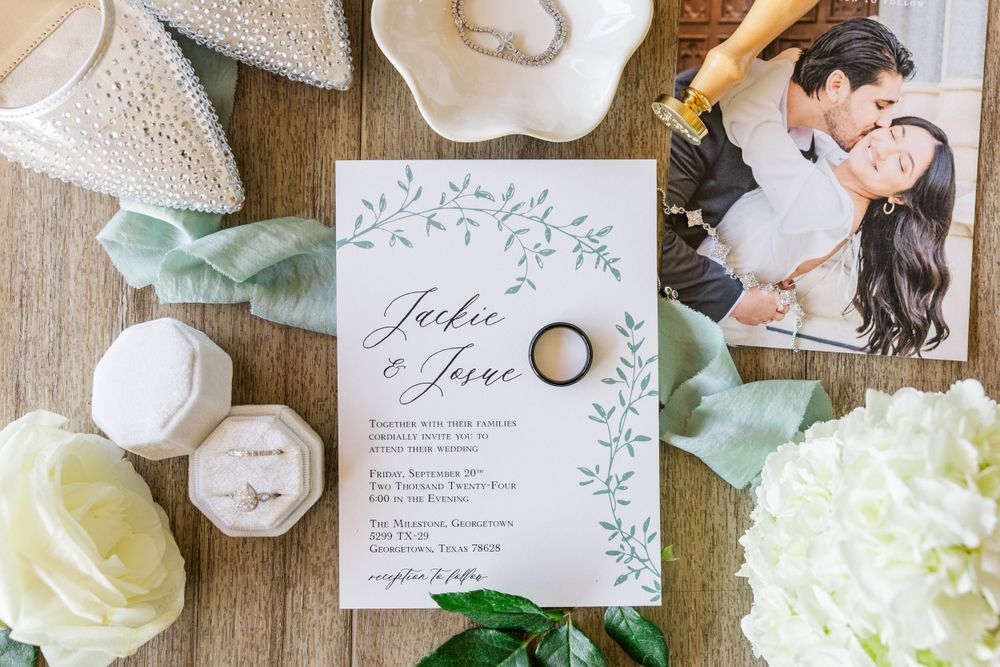 Wedding invitation with floral design surrounded by rings, flowers and decor elements on wooden surface.