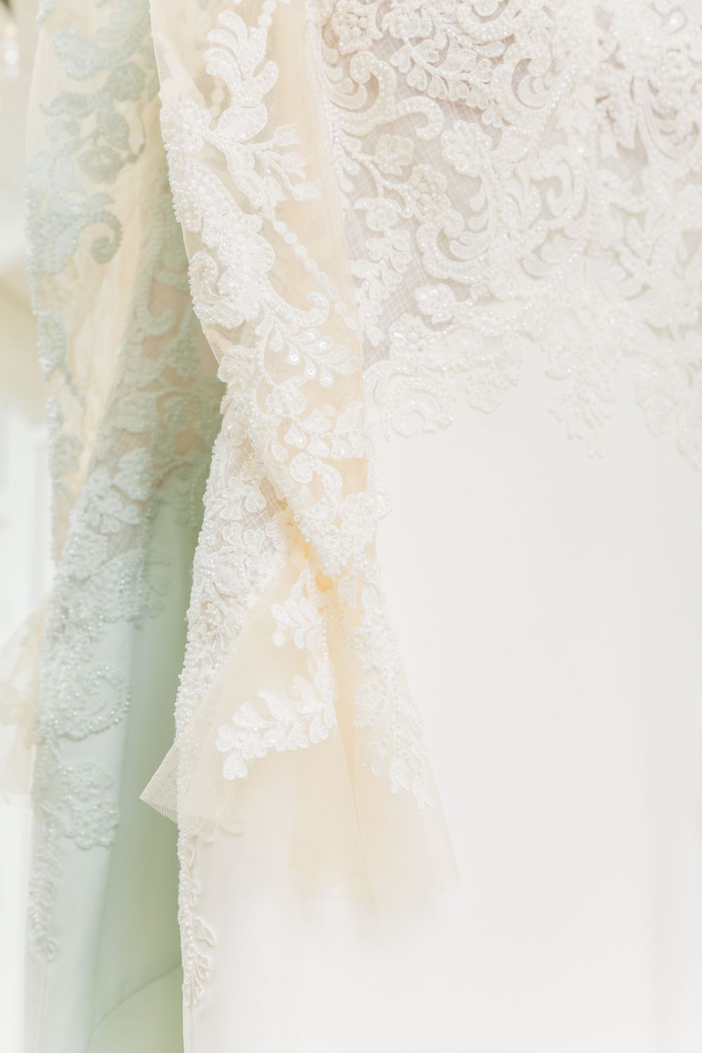 Close-up detail of delicate white lace and beading on an elegant wedding dress fabric.