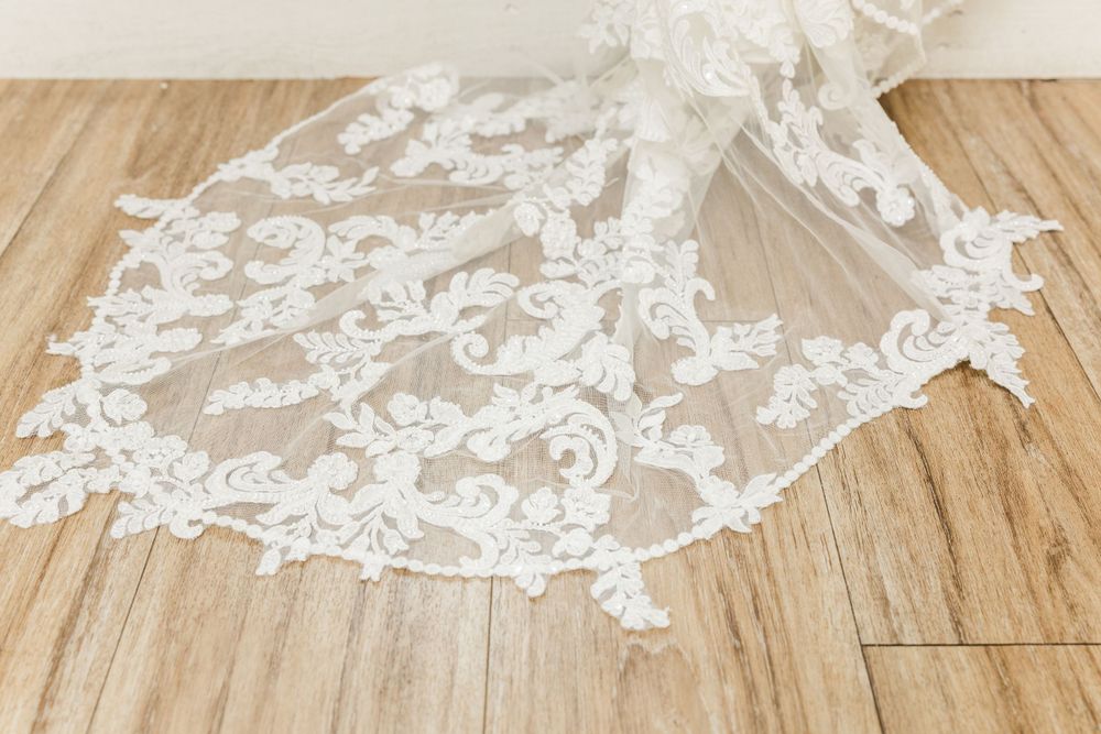 Delicate white lace detail of a wedding veil spread out on wooden flooring.