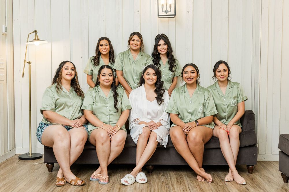 Bridal party in mint green robes sits together on couch during wedding preparations.