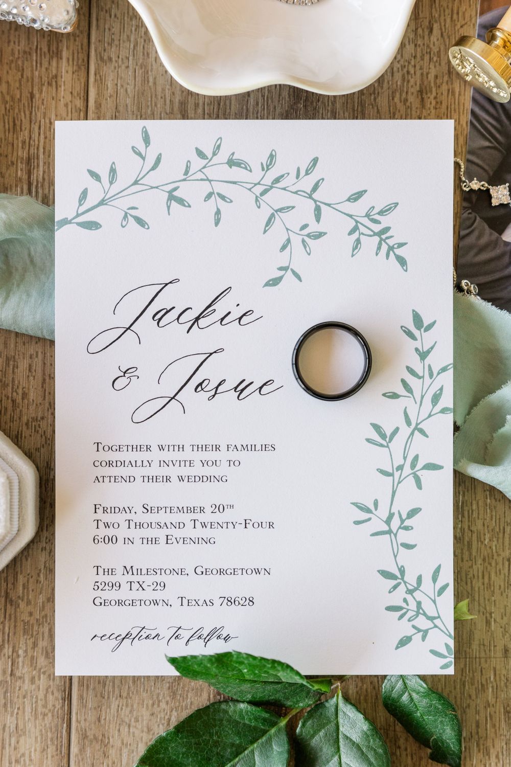 Elegant wedding invitation with delicate floral design and wedding ring on wooden surface.
