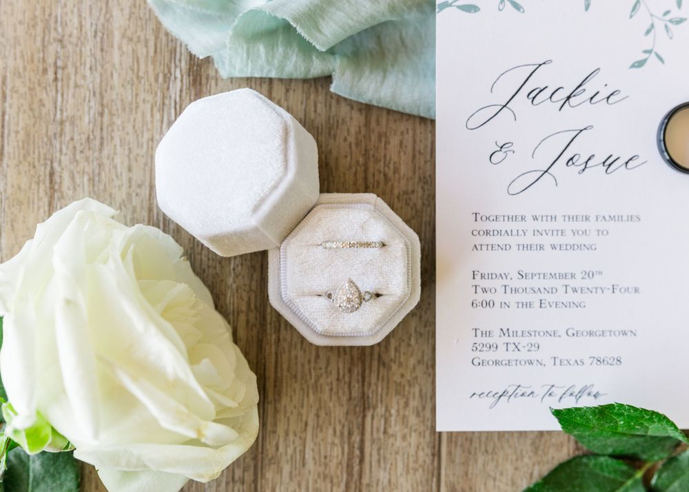 Wedding ring in velvet box with invitation and white flowers on wooden surface.