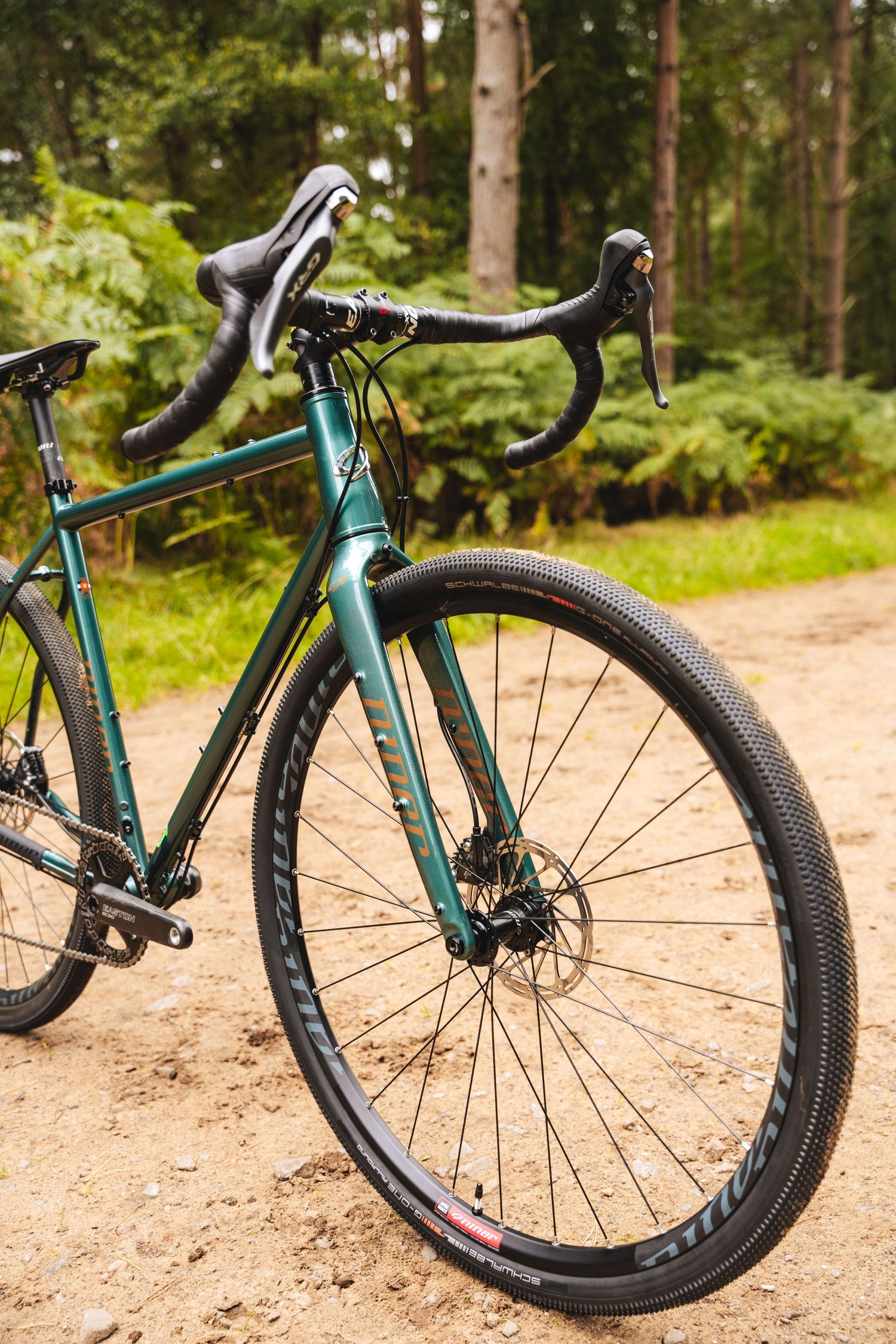 Front wheel and handlebar view of a green gravel bike with disc brakes on a forest trail.