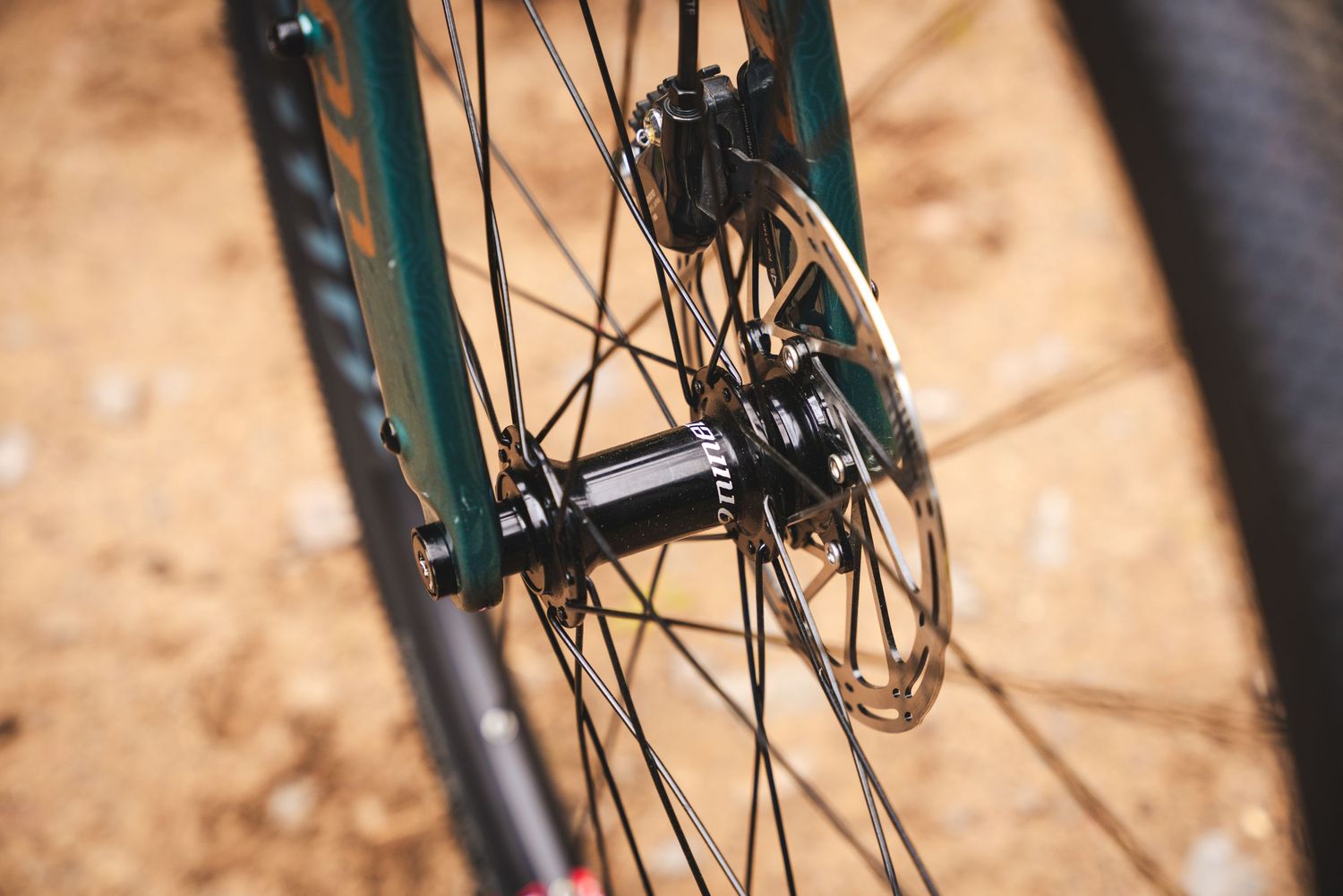 Close-up view of a bicycle wheel hub and spokes with disc brake mounted on turquoise frame.