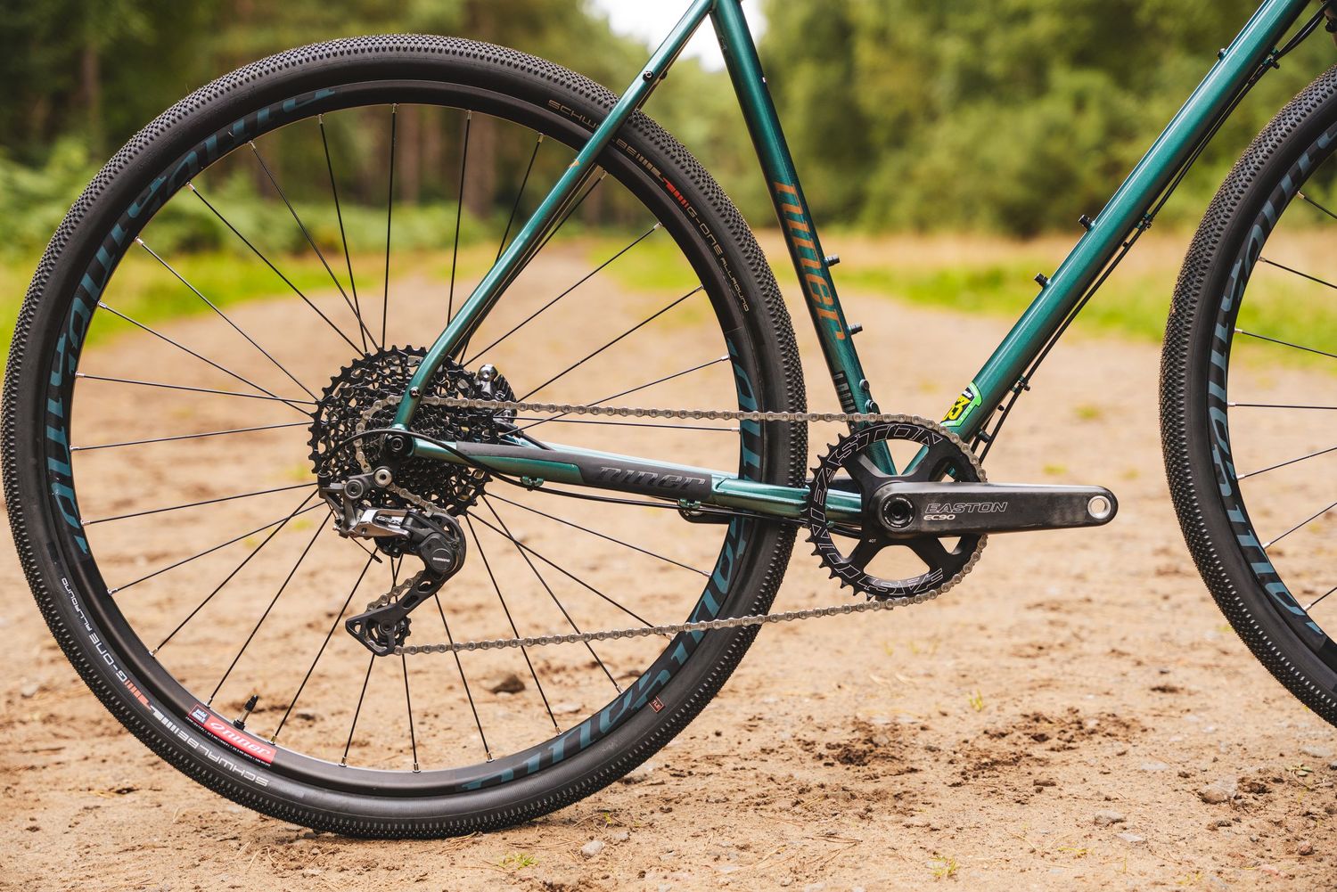 Close-up view of a green bicycle's rear wheel showing SRAM drivetrain components on a dirt trail.