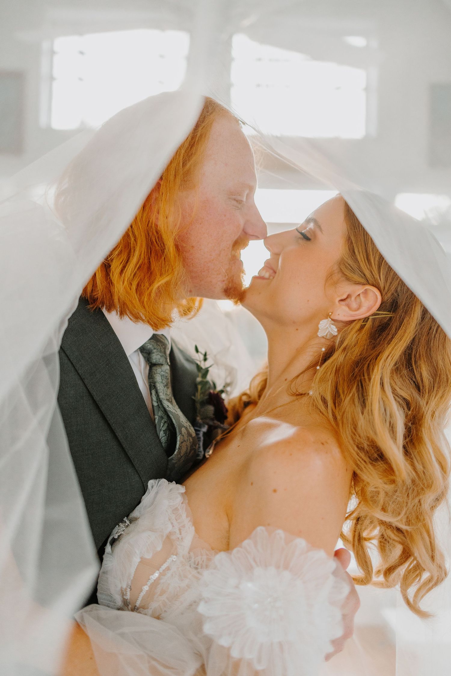 Romantic wedding couple shares intimate kiss in soft natural lighting.