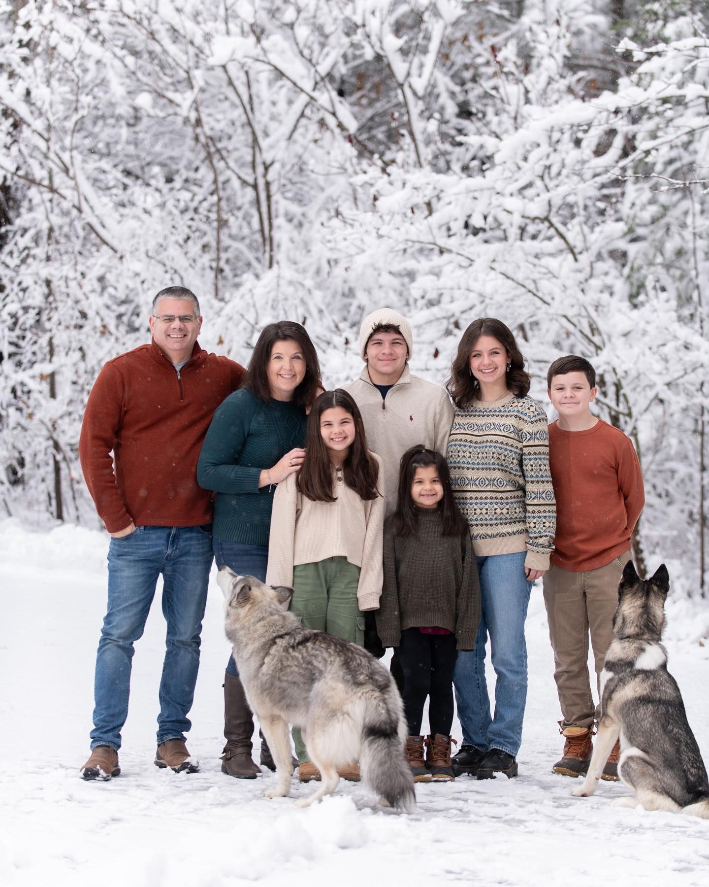 Family holiday photo with two huskies on grey couch near Christmas decorations.