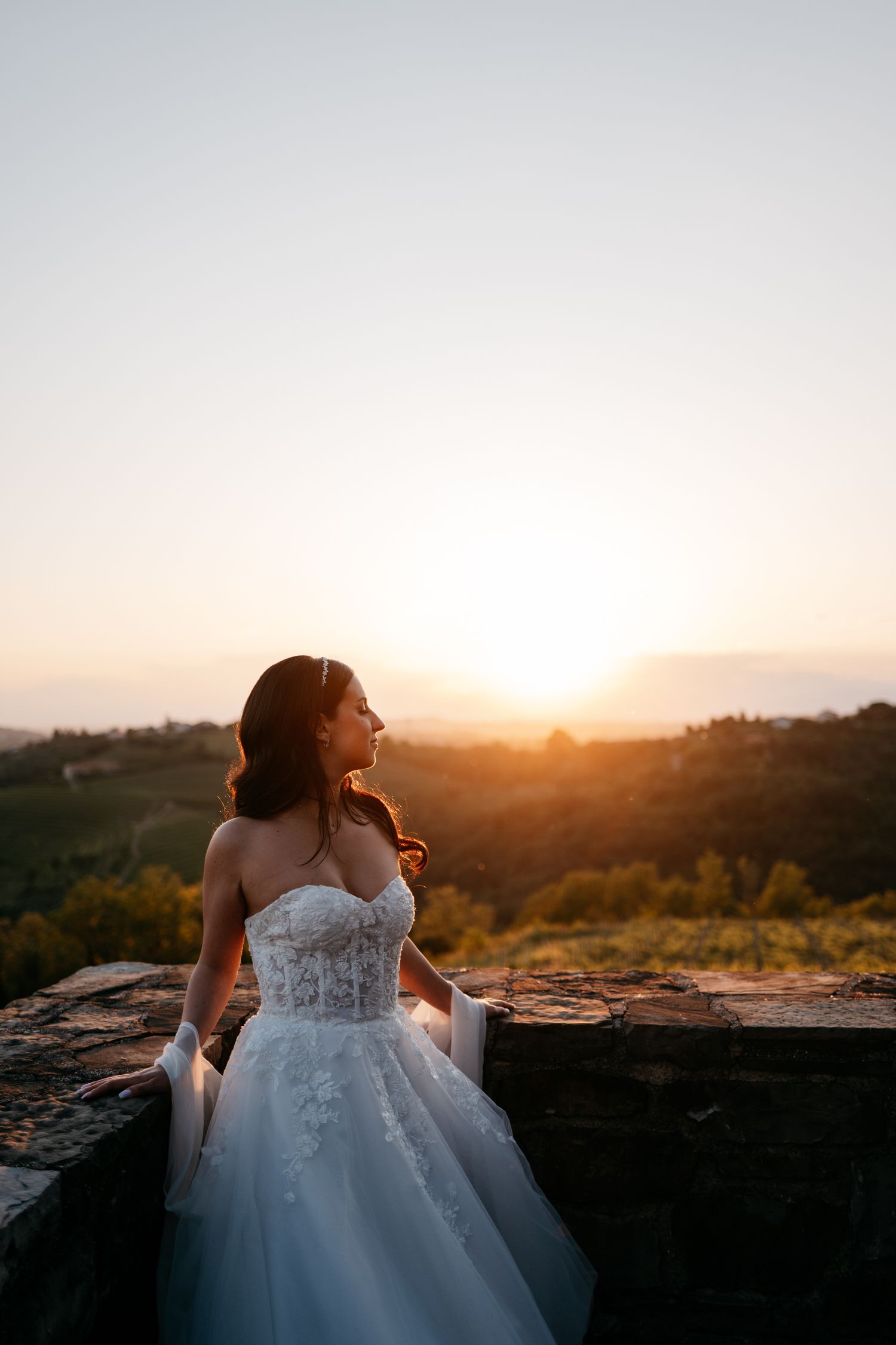 A bride in an elegant white wedding gown twirls in a grassy field at dusk, captured in black and white photography.