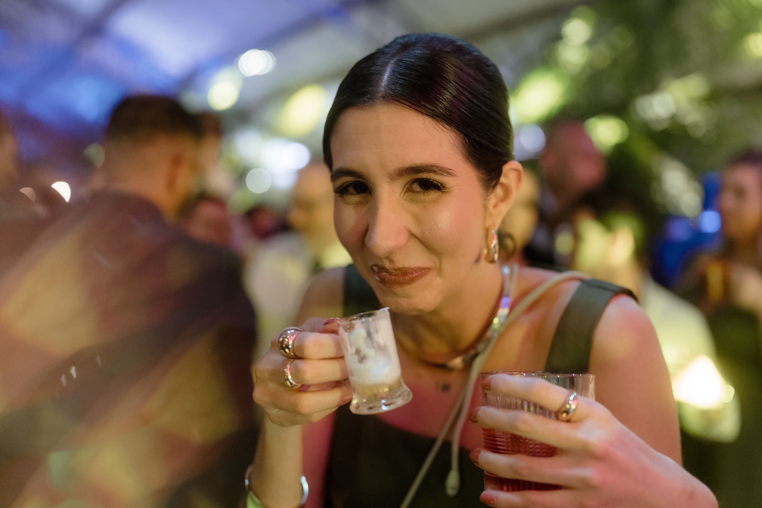 Person enjoying cocktails at outdoor evening party with festive lighting.