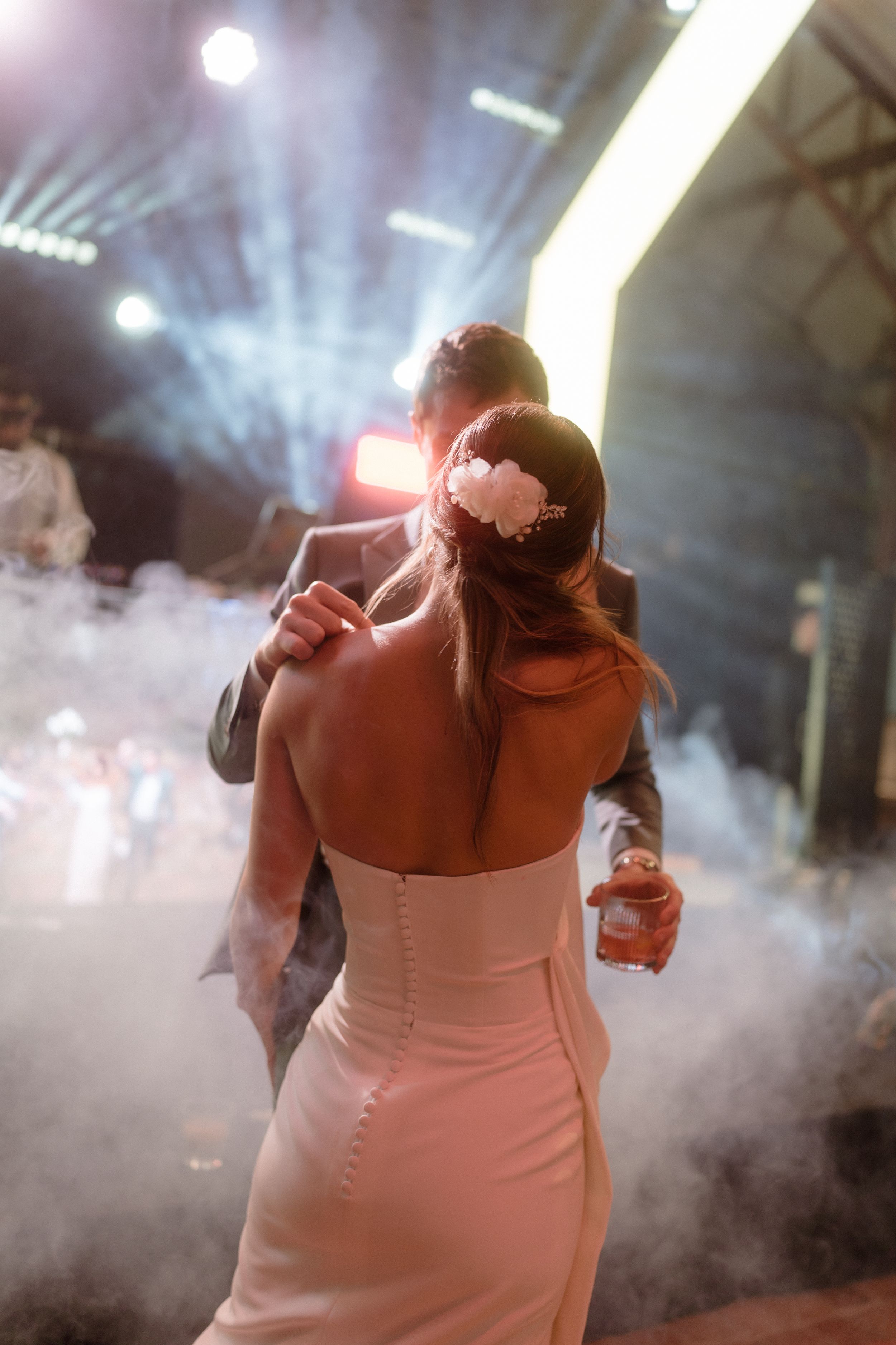 Couple dancing in white attire surrounded by atmospheric fog and stage lighting.