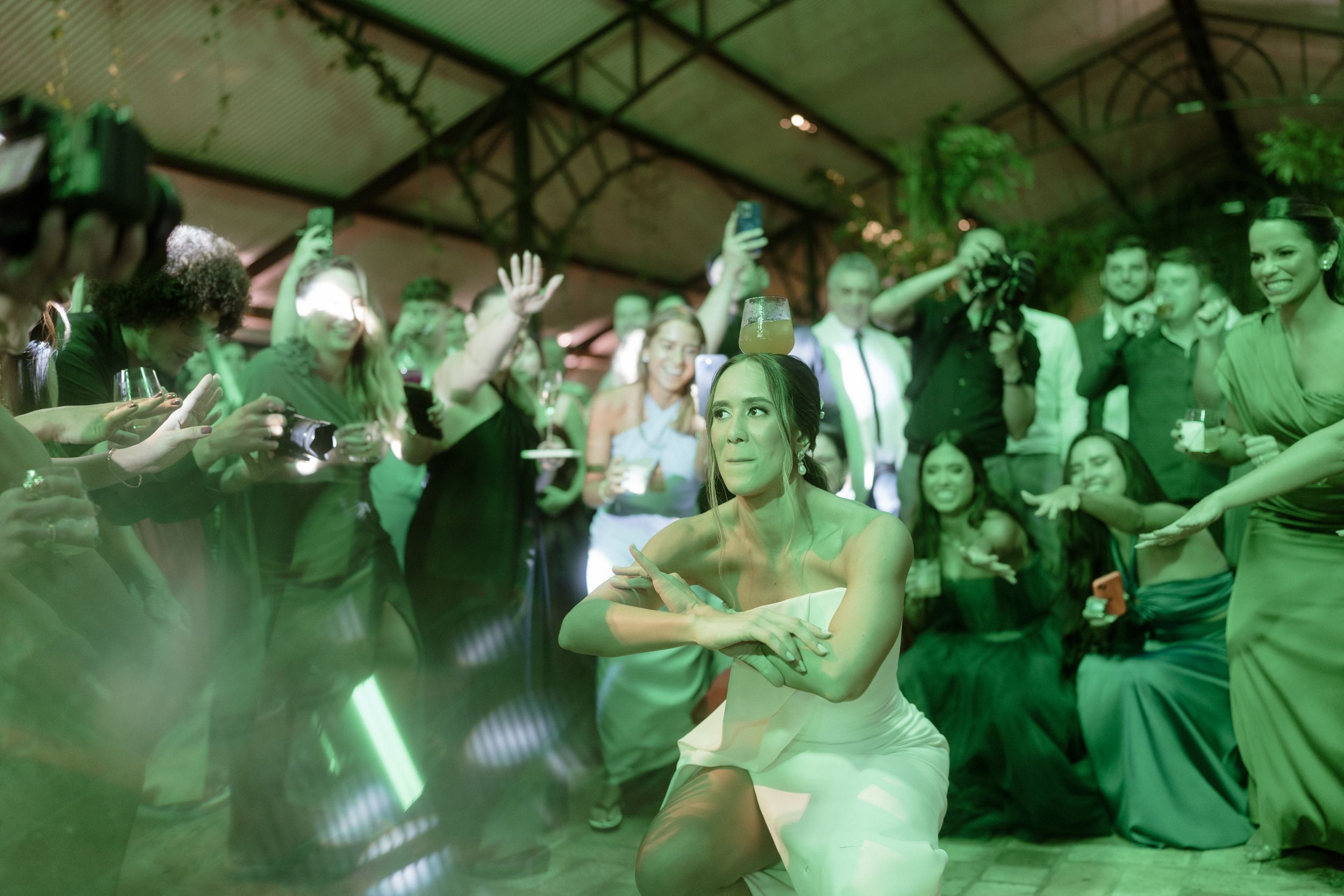 Guests dancing and celebrating under green atmospheric lighting at a reception venue.