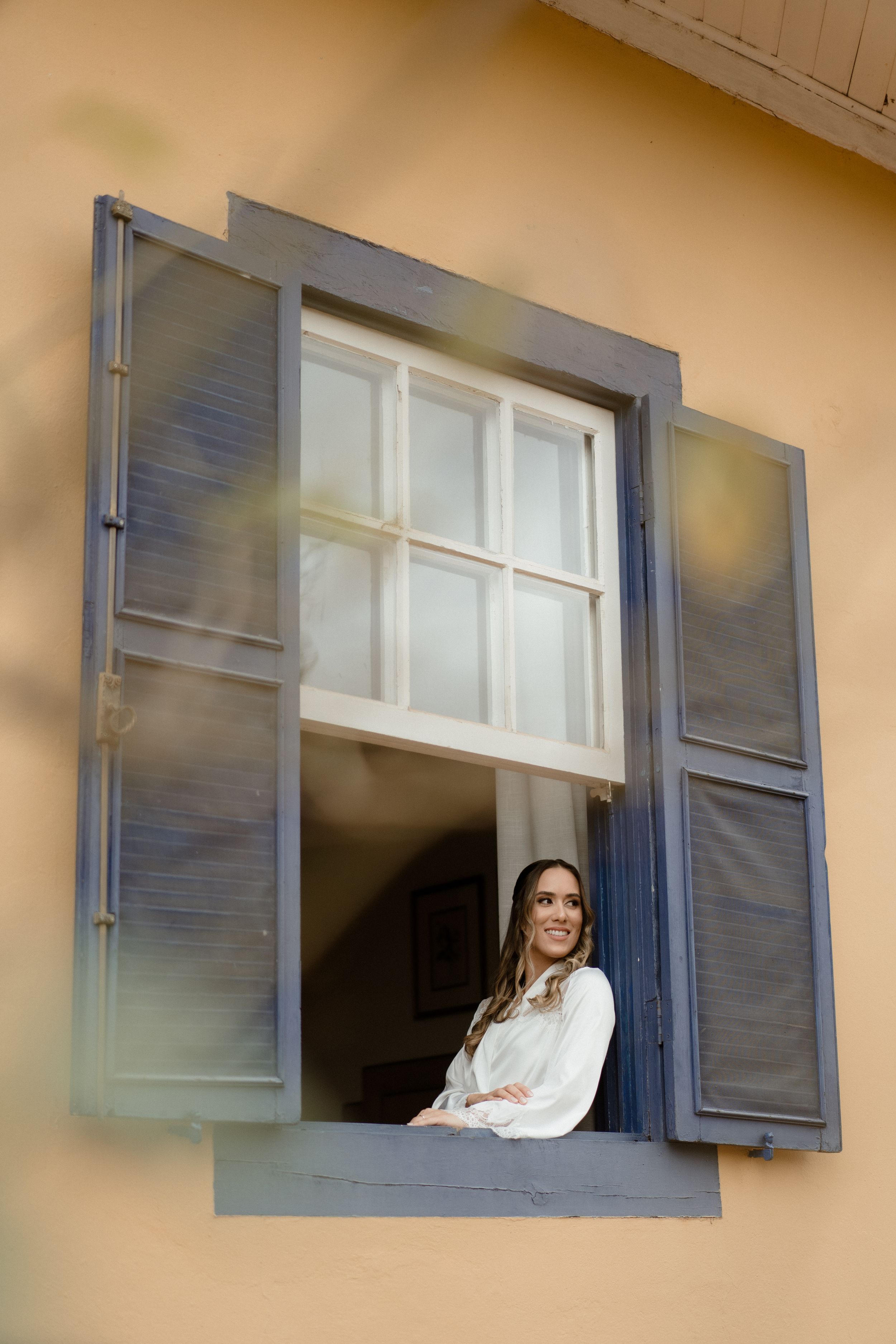 Light streams through open window shutters of a beige building.