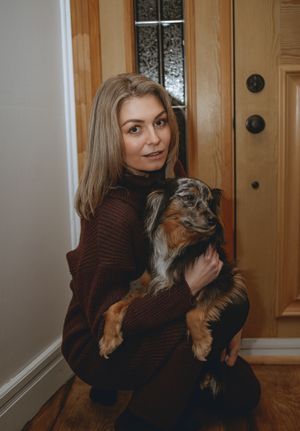 Australian shepherd sits with woman in burgundy sweater by front door.