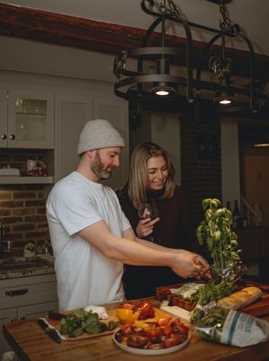 Couple preparing fresh vegetables in kitchen with wine and rustic decor.