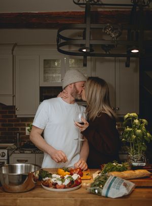Couple sharing intimate moment while cooking with fresh produce and wine.