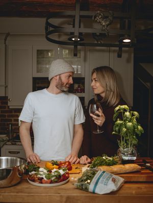 Couple enjoying wine while preparing fresh vegetables in rustic kitchen.