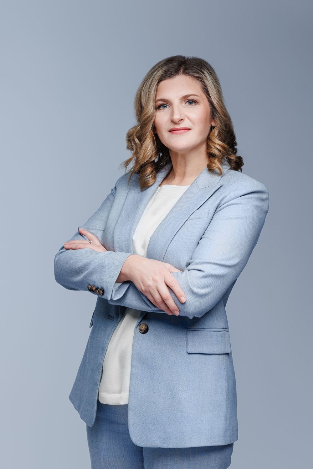 Professional headshot of woman in light blue blazer against grey background.