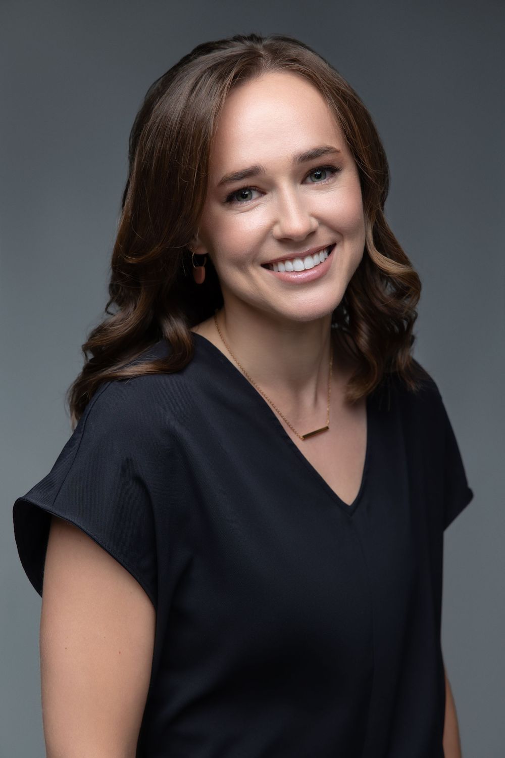 Professional headshot portrait of woman in black v-neck top with curled brown hair.