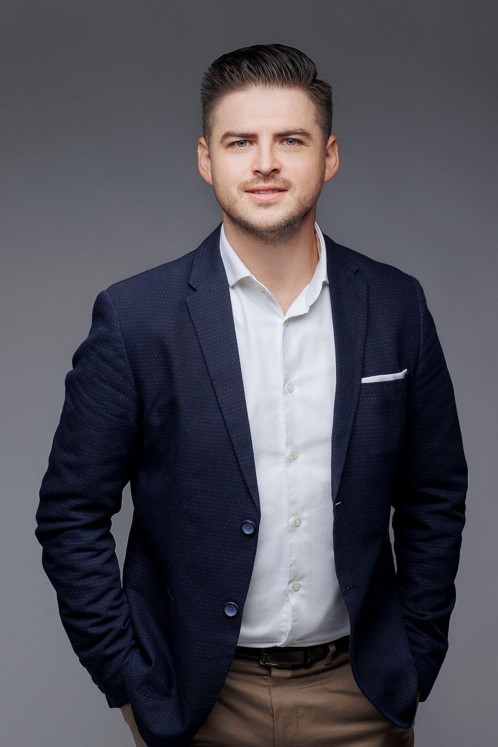 Business portrait of person in navy blazer and white shirt against grey backdrop.
