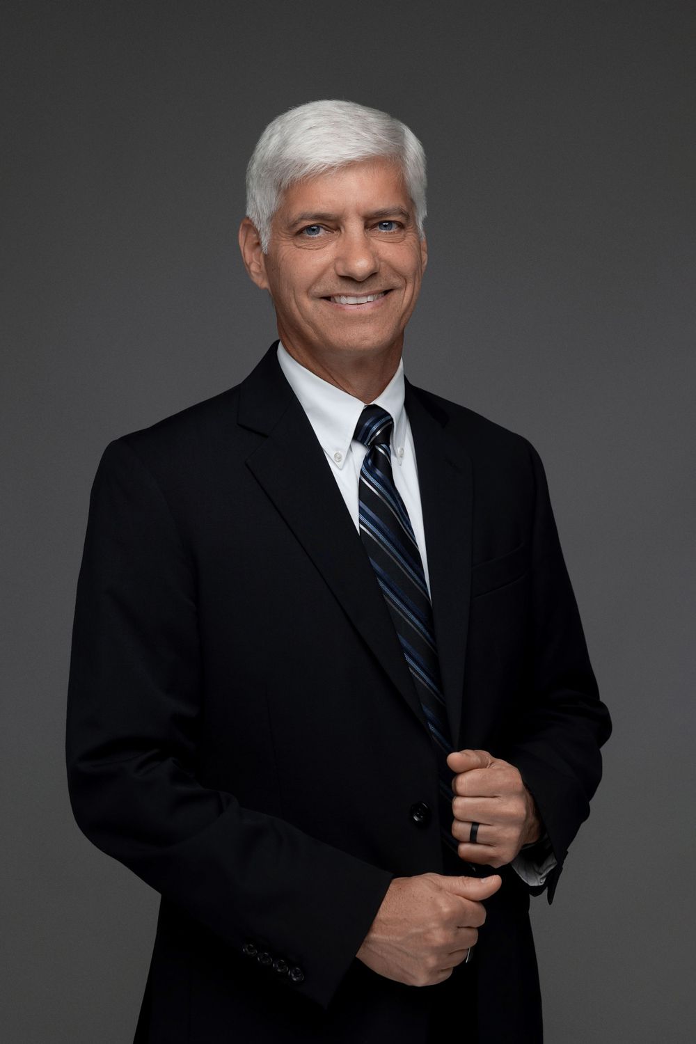 Professional portrait of person in black suit adjusting jacket.