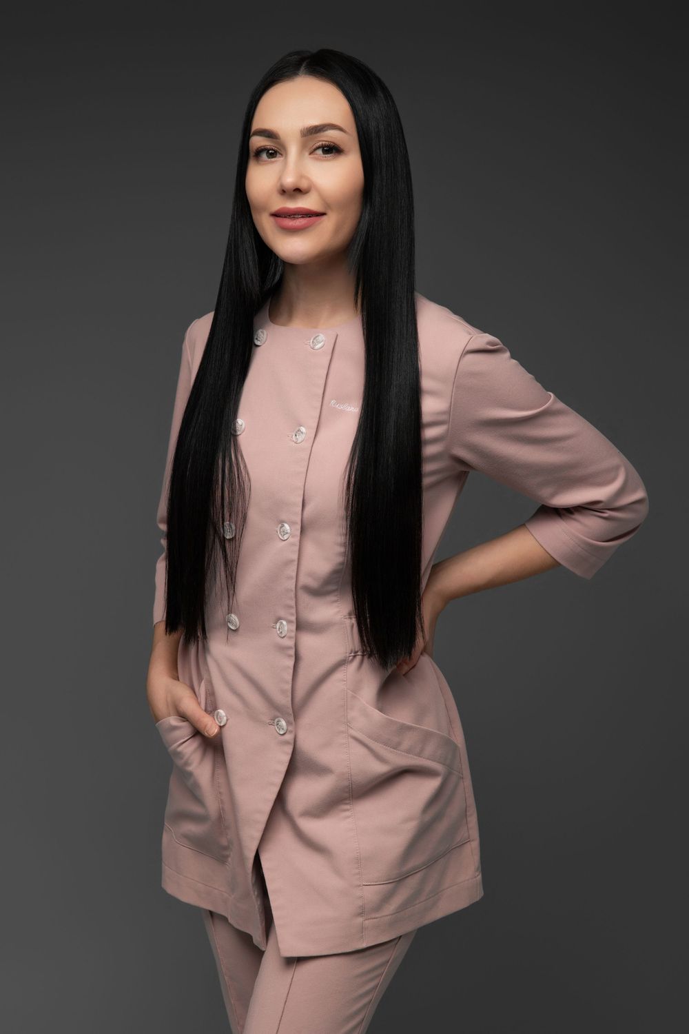 Professional photo of someone wearing a stylish pink medical uniform with long straight black hair against a dark background.