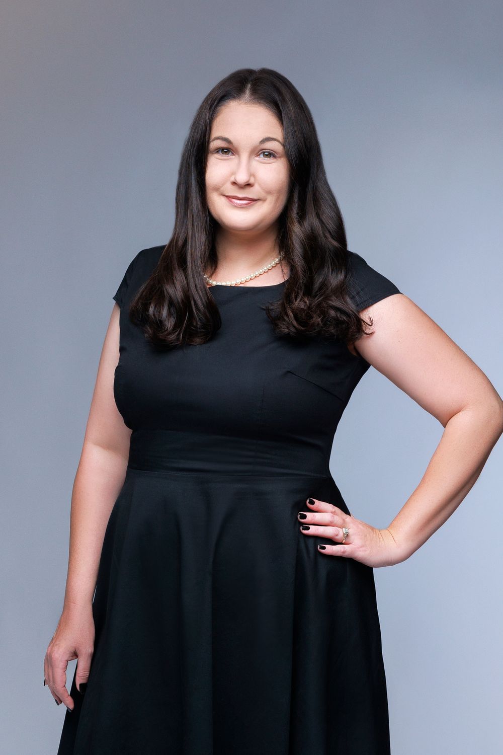 A professional studio portrait of a person wearing a sleek black sleeveless dress against a gray background.