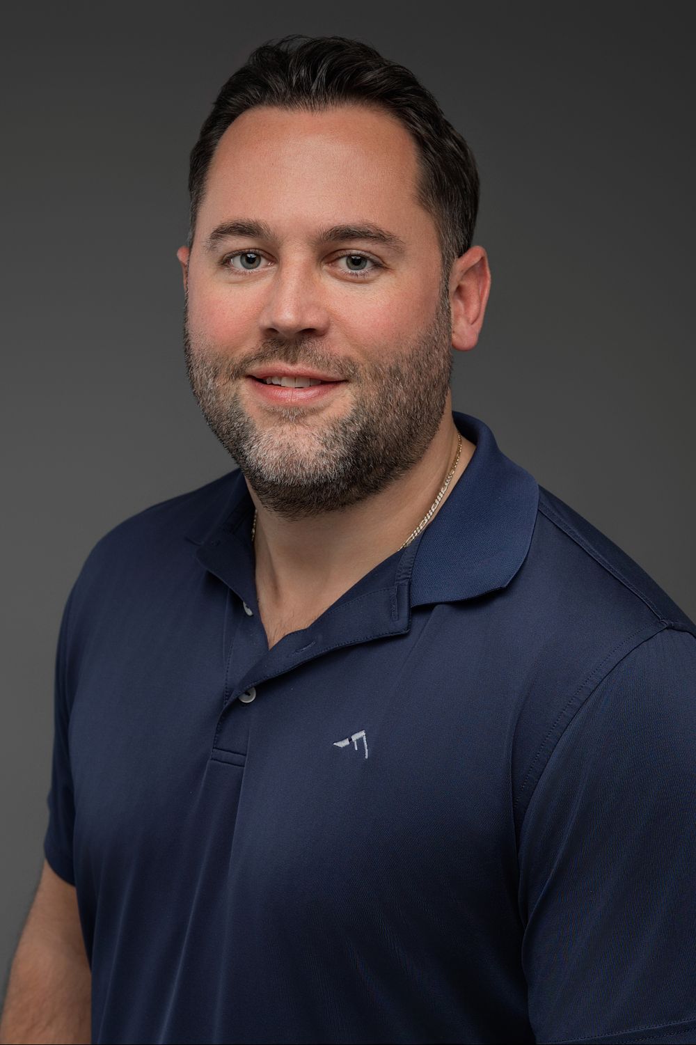Professional headshot of someone wearing a navy polo shirt against a dark gray background.