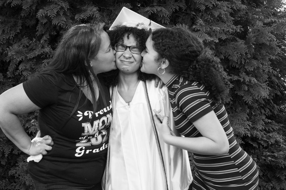 A touching graduation moment with celebratory kisses in black and white.