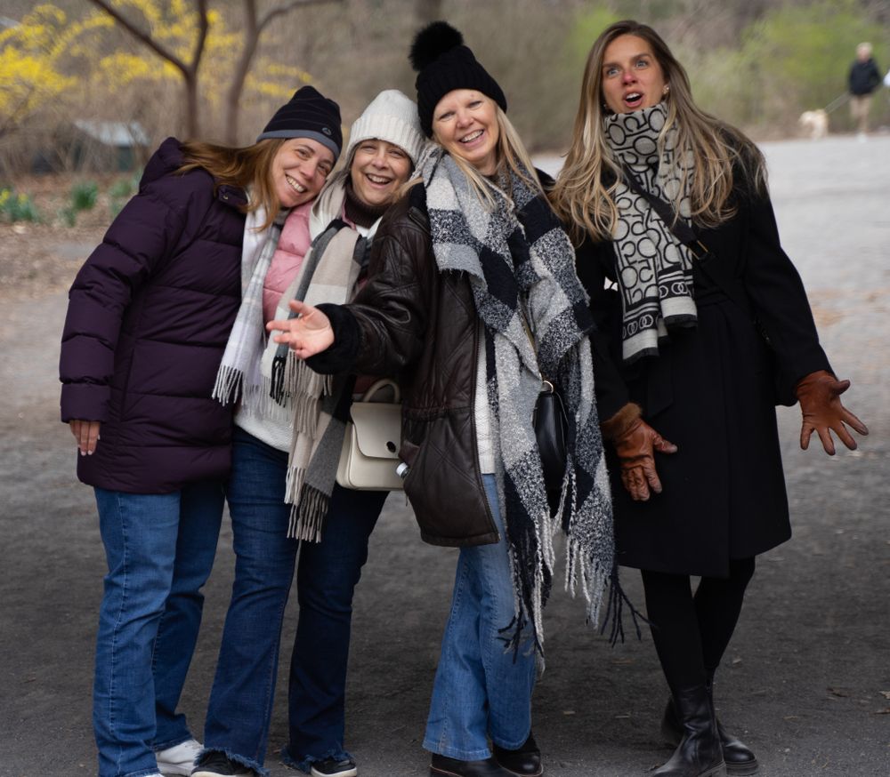 Four friends bundled up in winter coats and scarves pose together on a path during cold weather.