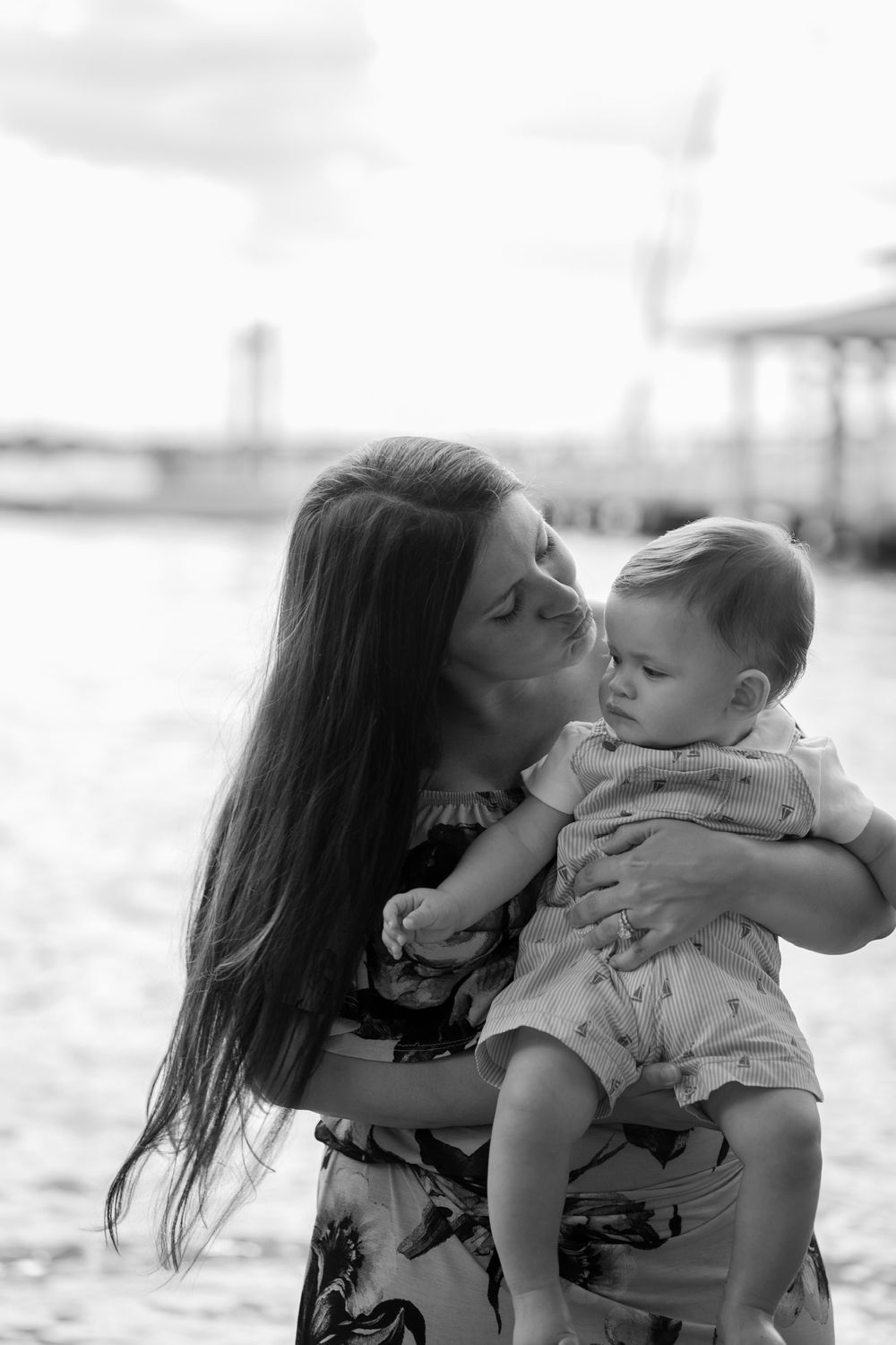 Mother and baby share tender moment during black and white beach photoshoot.