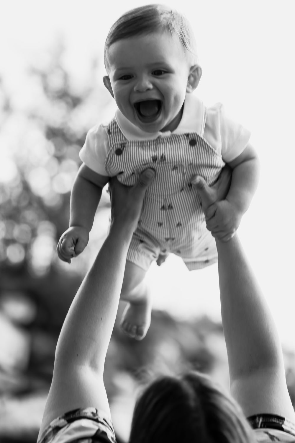 Black and white photo of joyful baby being lifted high in the air.
