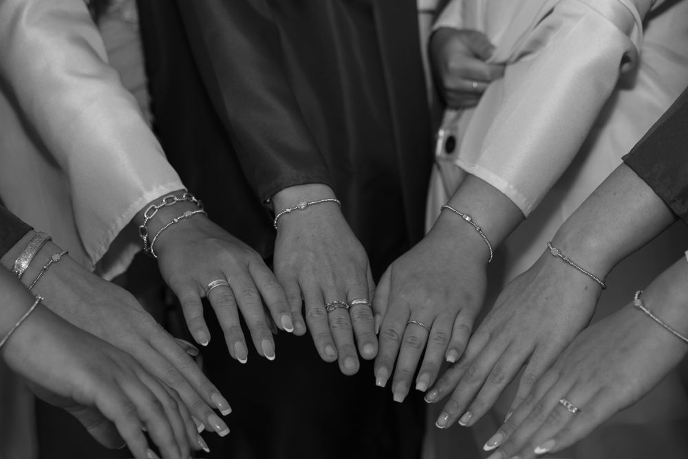 Black and white photo showing multiple hands with rings displayed in a circle.