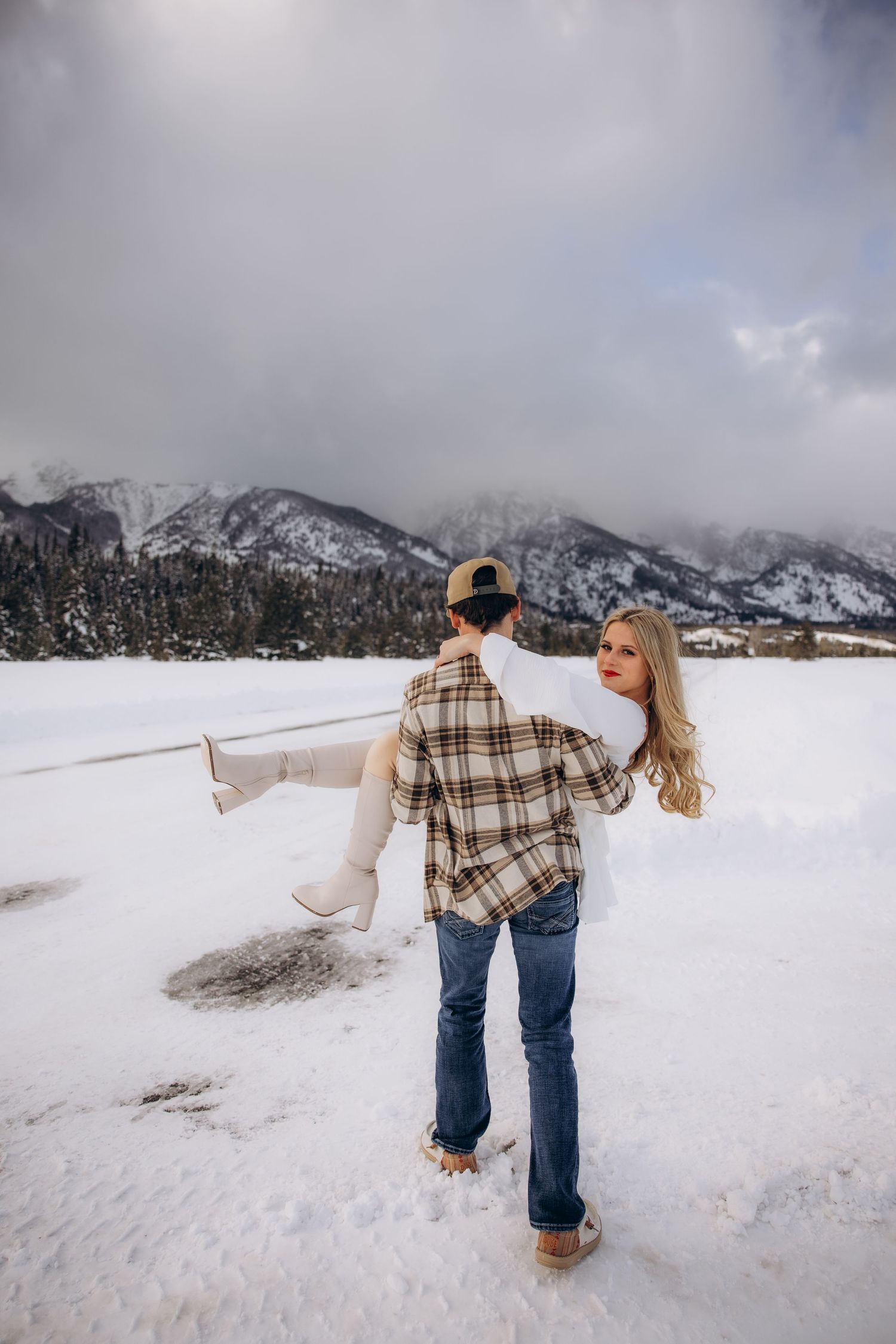 A couple dances together in the snow with snow-capped mountains in the background.