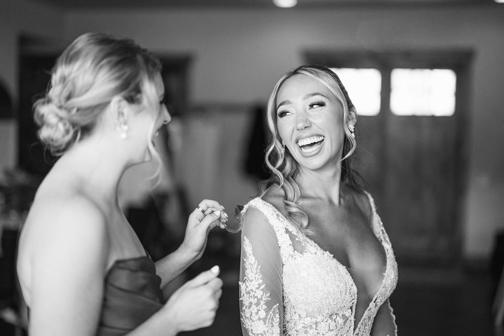 A bride in a white lace wedding dress laughs joyfully during a candid wedding moment.