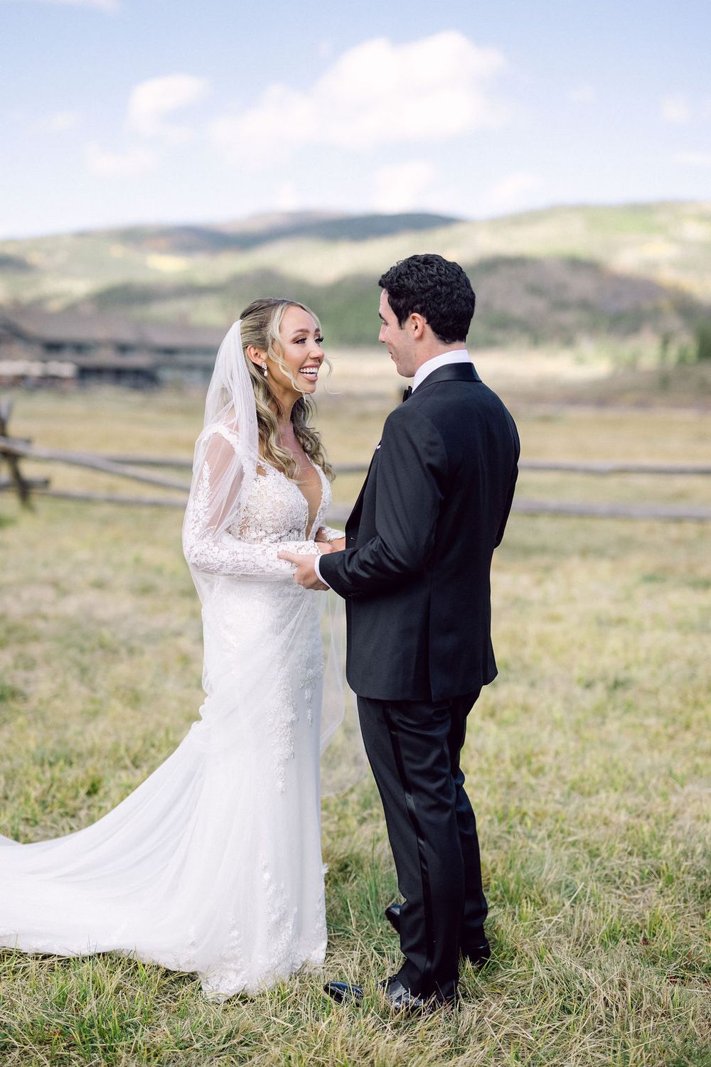A bride and groom share an intimate moment in a scenic mountain field during their wedding photoshoot.