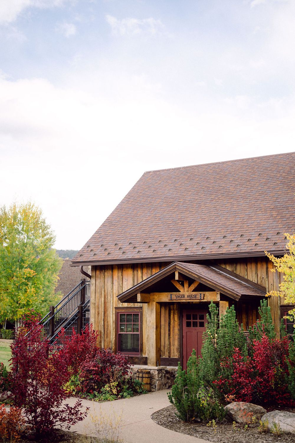 A rustic wooden barn-style building with red autumn foliage and landscaping shown from multiple exterior angles.