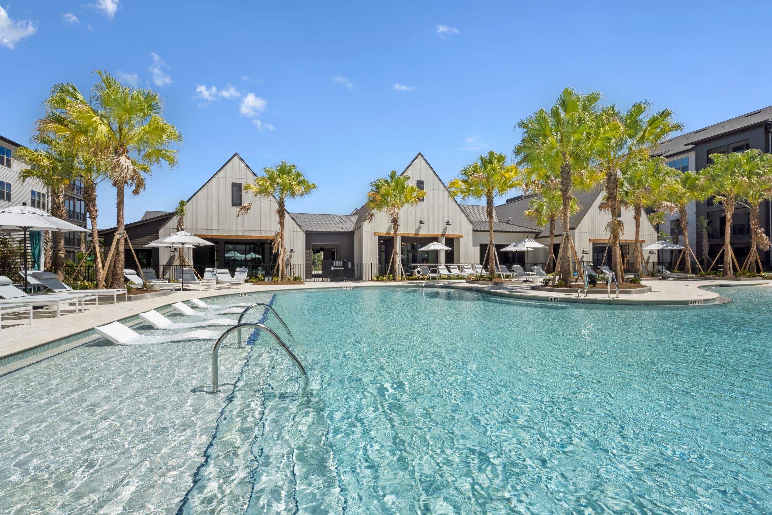 Luxury resort swimming pool surrounded by palm trees and modern cabanas with clear turquoise water and lounge areas.
