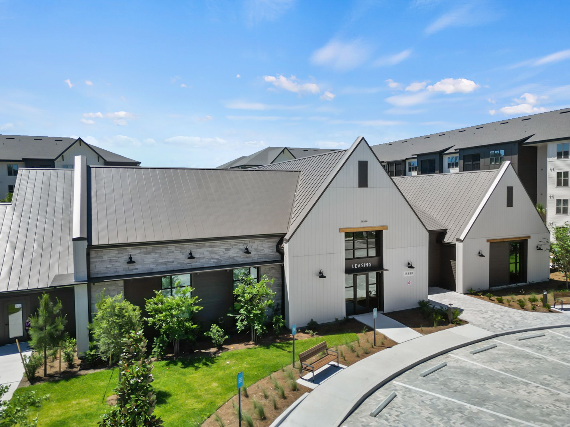 Modern apartment complex with white and grey exterior features peaked roofs and manicured landscaping under blue skies.