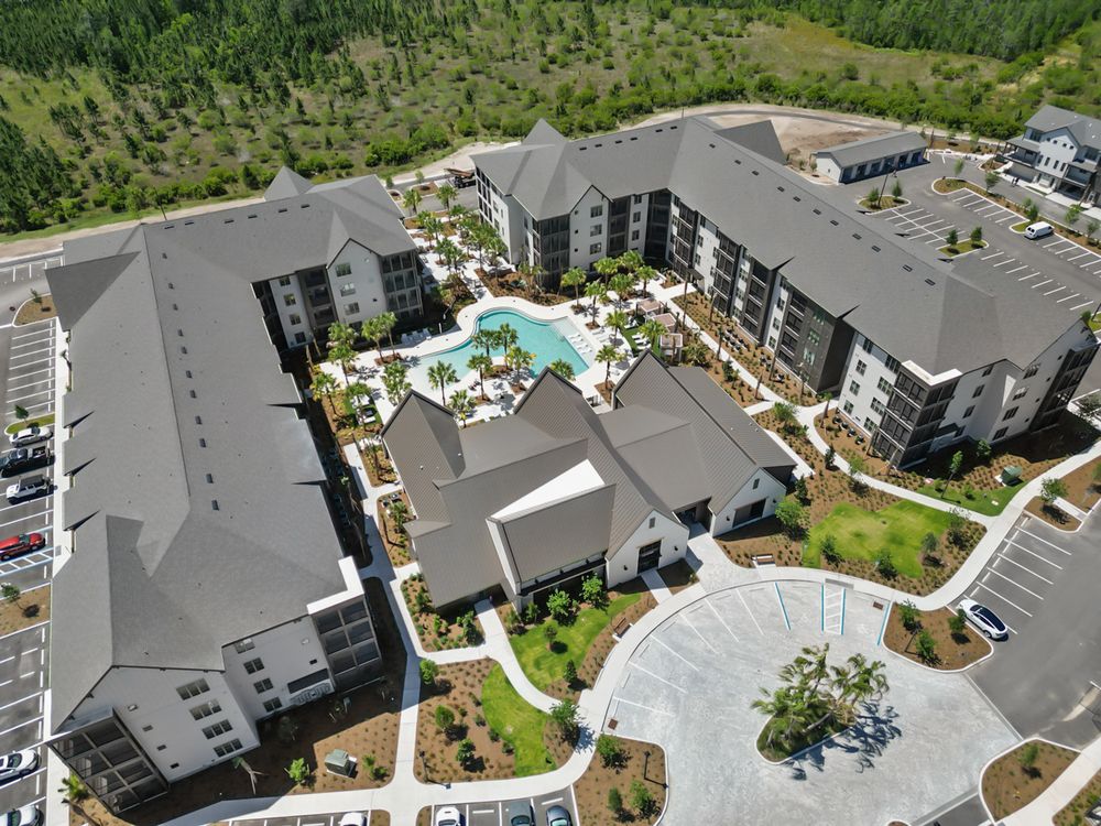 Aerial view of modern apartment complex with central swimming pool and grey roofs surrounded by trees.