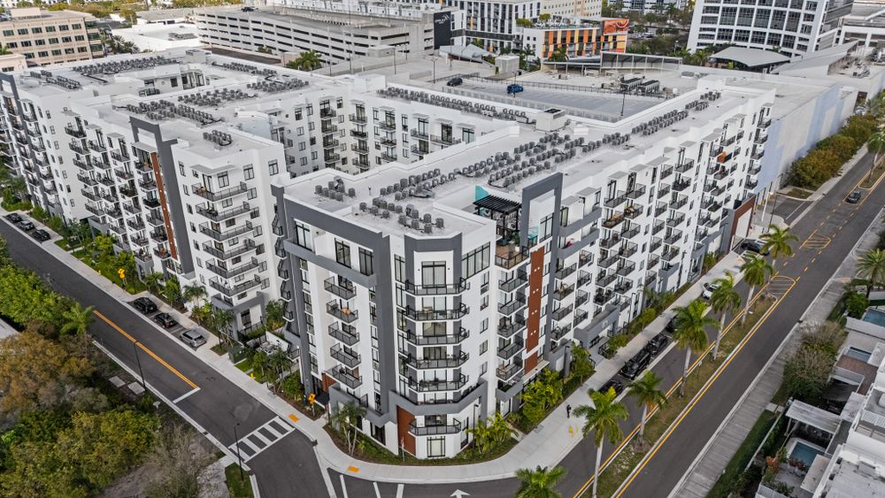 Modern white and gray apartment complex with curved corner architecture viewed from above in an urban setting.