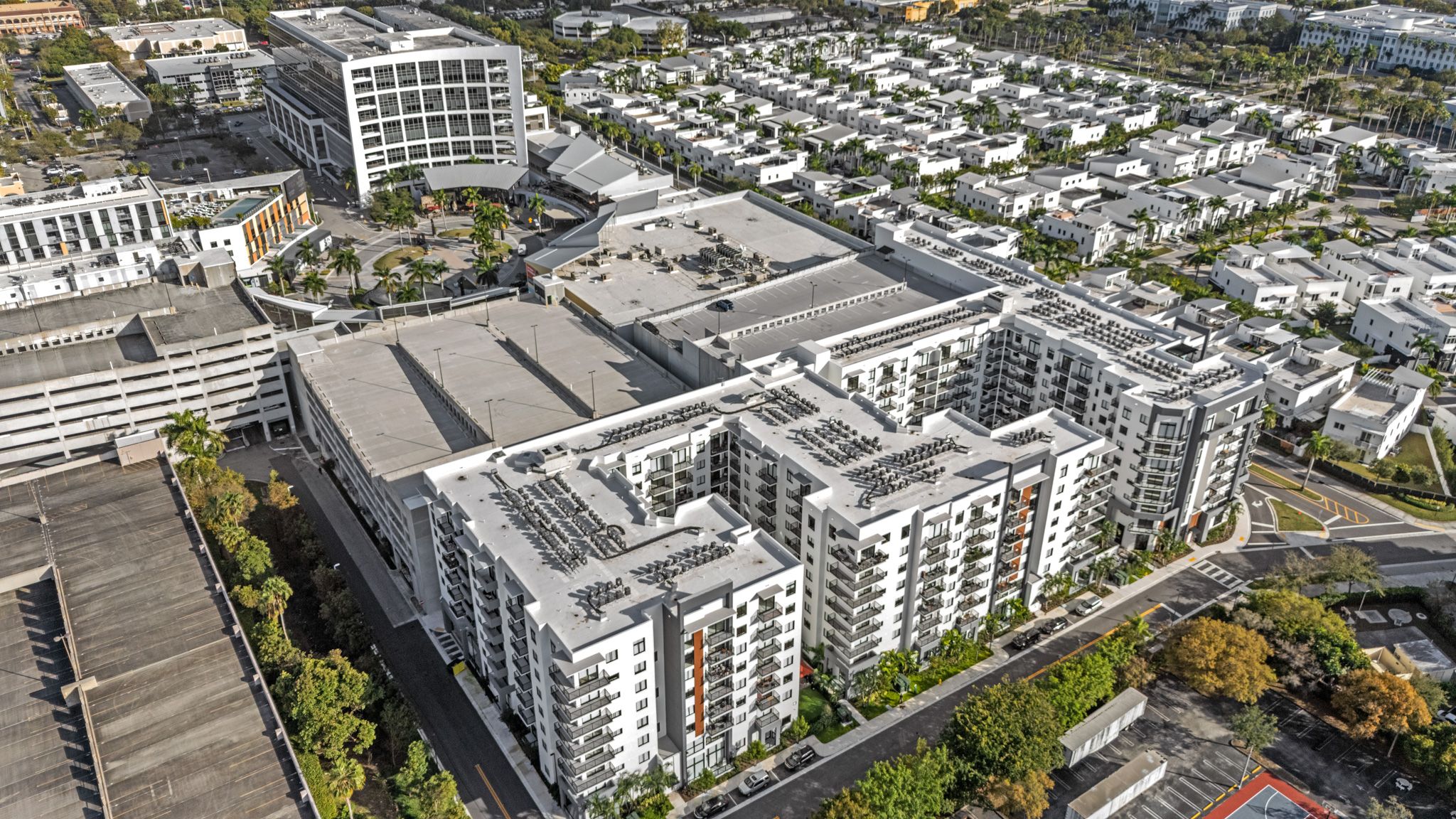 Aerial view of modern white apartment complex with surrounding residential neighborhoods and parking lots in an urban setting.
