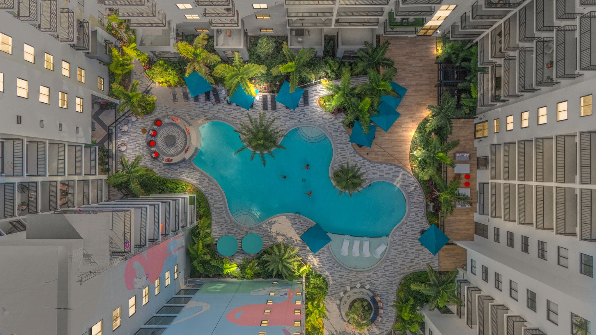 Aerial view of a tropical-style swimming pool surrounded by modern apartment buildings and lush landscaping.