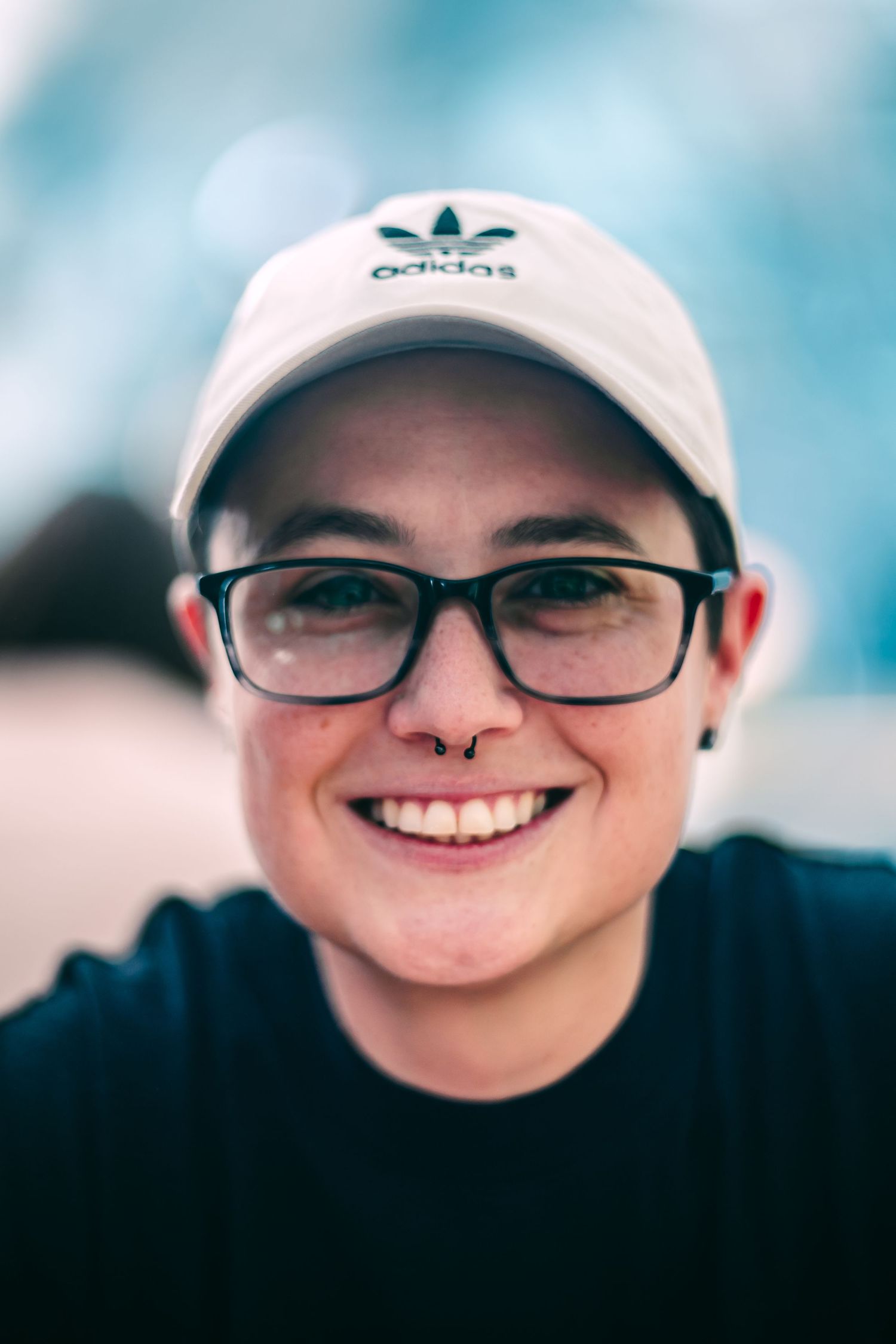 Close-up portrait wearing an Adidas cap, glasses and a warm smile.