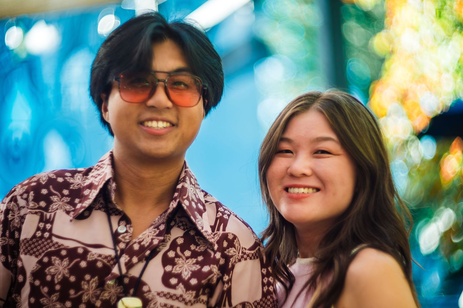 Candid photo of a happy couple smiling together outdoors with colorful bokeh background.