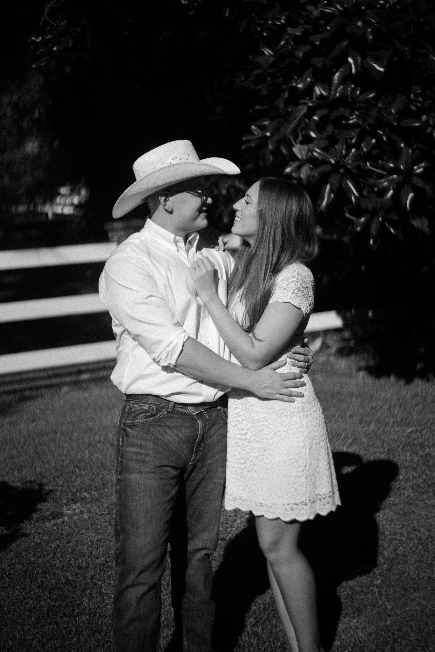 A romantic black and white photo of a couple embracing outdoors in western attire.