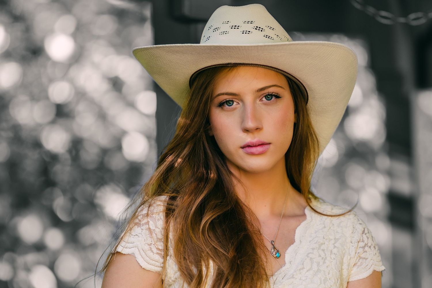 Portrait of someone in a cream cowboy hat and lace dress against a blurred background.